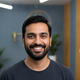 Portrait of a smiling South Asian man in his 30s, looking confidently at the camera, conveying trust and happiness. The backg